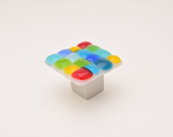 May include: Square cabinet knob with a white base and a colorful glass top. The glass top features a mosaic of small, round, colored glass pieces in shades of blue, green, yellow, and red.