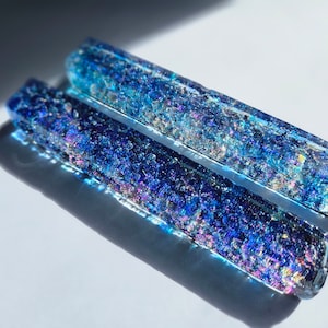 Può includere: Due aste di vetro iridescente con sfumature blu e viola. Il vetro è pieno di piccole particelle scintillanti.