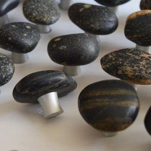 May include: A collection of smooth, black and gray stone drawer pulls with silver metal bases. The stones are various shapes and sizes.