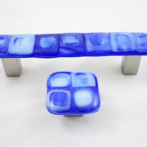 Puede incluir: Un juego de dos pomos de armario de vidrio azul y blanco con un patrón geométrico. Los pomos son de vidrio y tienen una base de metal plateado.