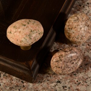 May include: Three pink and green granite stone cabinet knobs. The knobs are round and have a smooth, polished finish.
