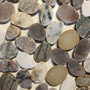 May include: A collection of smooth, oval-shaped river rocks in various shades of grey, brown, and white. The stones are arranged in a random pattern on a white background.