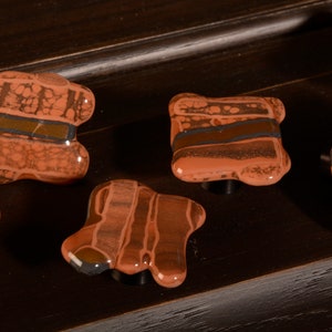 Könnte beinhalten: Fünf braune und orangefarbene Keramik-Schrankknöpfe mit einem marmorierten und gestreiften Muster. Die Knöpfe sind unregelmäßig geformt und haben eine glänzende Oberfläche.
