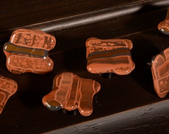 Könnte beinhalten: Fünf braune und orangefarbene Keramik-Schrankknöpfe mit einem marmorierten und gestreiften Muster. Die Knöpfe sind unregelmäßig geformt und haben eine glänzende Oberfläche.