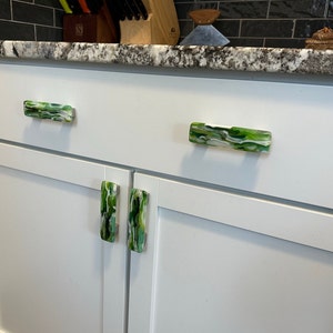 May include: White kitchen cabinets with green and white glass drawer pulls.