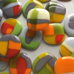 May include: A collection of colourful glass tiles with geometric patterns in shades of grey, green, yellow, orange, and white.