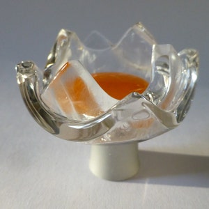 May include: A clear glass flower-shaped dish with an orange liquid inside. The dish has a white base.