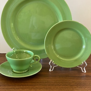 May include: A set of green ceramic dinnerware, including a large plate, a smaller plate, a teacup, and a saucer.