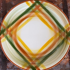 May include: A white ceramic plate with a brown, yellow, and green plaid design. The plate has a slightly raised rim and a smooth, glossy finish.