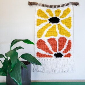 Pu&ograve; includere: Un arazzo da parete all'uncinetto con due grandi fiori stilizzati. Il fiore superiore &egrave; giallo e il fiore inferiore &egrave; arancione. Entrambi i fiori hanno centri neri.