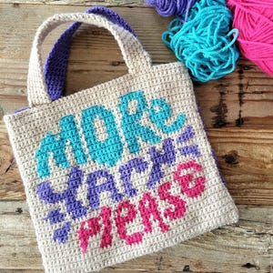 May include: A beige crochet tote bag with the words "MORE YARN PLEASE" in turquoise, purple, and pink. The bag has purple handles and is surrounded by colorful yarn.