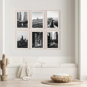 May include: A set of six black and white photographs of Chicago cityscapes. The photos are framed in a light wood frame and are arranged in a grid pattern on a white wall. The photos show different views of the city, including the skyline, the river, and the streets.