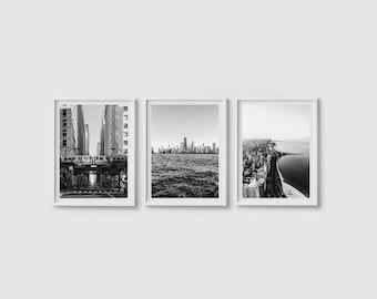 Op de afbeelding: Set van drie ingelijste zwart-witfoto's. Eén toont een stadsstraat met een trein, een andere een skyline over water en de derde een luchtfoto van een stad en kustlijn. De frames zijn wit.