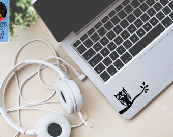 May include: A laptop with a black and white owl decal on the lower right corner. White headphones are next to the laptop. The text "LONDON'S FINEST DECAL SHOP" is in a blue rectangle in the upper left corner.