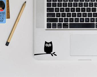 May include: A black and white owl silhouette sticker on a silver laptop. The owl is perched on a branch with its wings spread out.