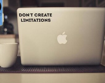 May include: A silver laptop with the Apple logo, a white coffee cup, and the text "DON'T CREATE LIMITATIONS". The laptop sits on a brown mat. A decal shop logo is in the background.