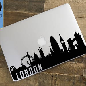 Peut inclure: Silhouette noire de l'horizon de Londres sur un ordinateur portable. Le design comprend des monuments embl&eacute;matiques tels que le London Eye, Big Ben et le Tower Bridge. Le mot "LONDON" est imprim&eacute; en blanc. Le logo "LONDON'S FINEST DECAL SHOP" est &eacute;galement visible.