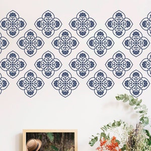Pode incluir: Um padrão repetitivo de quatro folhas florais azuis escuros adorna uma parede branca. O design é uma borda decorativa, adequada para decoração de casa. A imagem também inclui uma imagem emoldurada e um arranjo floral com vegetação.