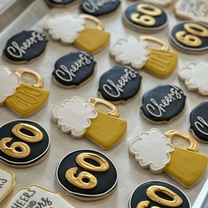 May include: A collection of decorated sugar cookies with various designs, including beer mugs, the number 60, and the phrase "Cheers and Beers to 60 Years". The cookies are arranged on a baking sheet.