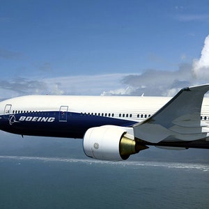 K&ouml;nnte beinhalten: Ein wei&szlig;es und blaues Boeing 787 Dreamliner Flugzeug im Flug &uuml;ber einem Gew&auml;sser. Das Flugzeug hat markante Winglets an den Fl&uuml;geln.