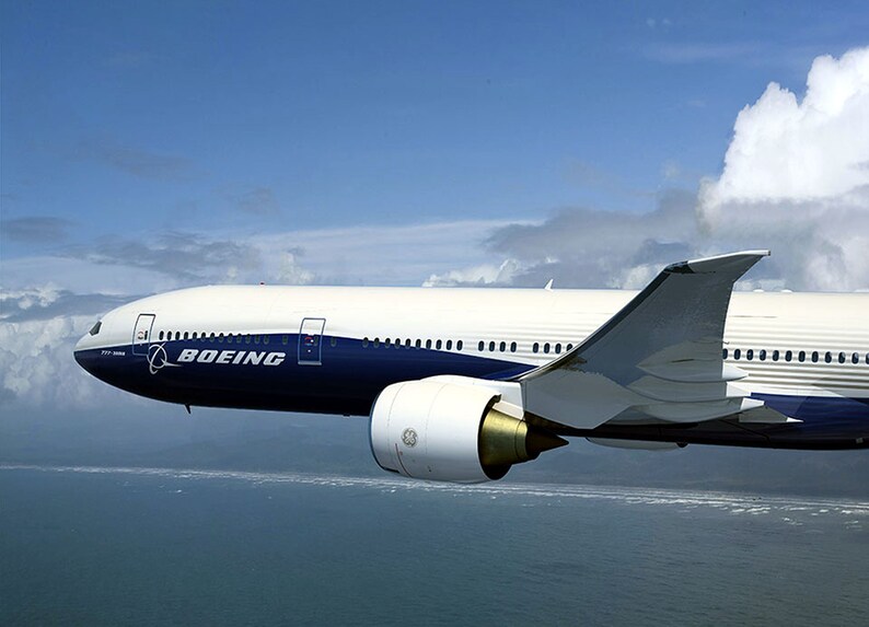 K&ouml;nnte beinhalten: Ein wei&szlig;es und blaues Boeing 787 Dreamliner Flugzeug im Flug &uuml;ber einem Gew&auml;sser. Das Flugzeug hat markante Winglets an den Fl&uuml;geln.