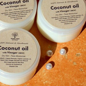 May include: Three glass jars of coconut oil with vinegar, labeled "Coconut oil with Vinegar (acv)" and "100% Natural & Handmade". The jars are on a textured orange surface with white pearl beads scattered around them.