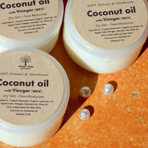 May include: Three jars of coconut oil with vinegar face moisturizer. The jars are labeled "Coconut oil with Vinegar (acv)" and "100% Natural & Handmade". The jars are on a brown surface with white pearl beads.
