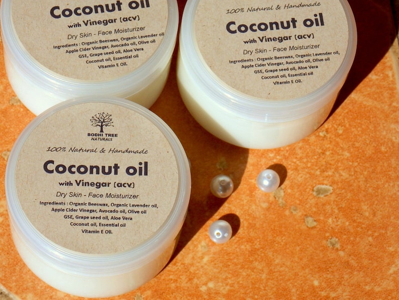 May include: Three jars of coconut oil with vinegar face moisturizer. The jars are labeled "Coconut oil with Vinegar (acv)" and "100% Natural & Handmade". The jars are on a brown surface with white pearl beads.