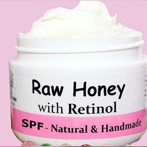 May include: A white jar with a pink label that reads "Raw Honey with Retinol SPF - Natural & Handmade".