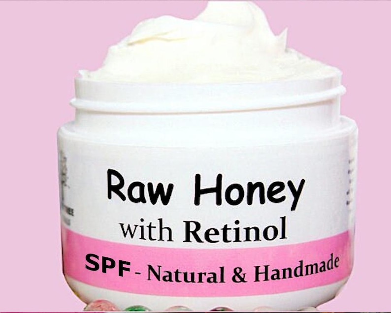 May include: A white jar with a pink label that reads "Raw Honey with Retinol SPF - Natural & Handmade".