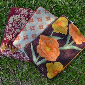 Puede incluir: Tres bolsas de tela acolchadas con diferentes patrones. La primera bolsa es roja con un diseño floral blanco, la segunda es beige con un patrón geométrico rojo y blanco, y la tercera es marrón con un diseño floral en tonos naranja y amarillo.