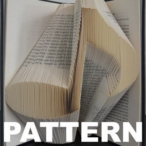 May include: A book art sculpture made by folding the pages of a book into a geometric pattern. The book is open and the pages are folded to create a three-dimensional shape. The word "PATTERN" is printed in white letters at the bottom of the image.