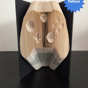 Könnte beinhalten: Ein Buch, das zu einem Videospiel-Controller gefaltet ist. Der Controller ist aus beigefarbenem Papier und hat einen schwarzen Hintergrund. Das Buch steht auf einer schwarzen Oberfläche.