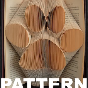 May include: A book art project, also known as book folding, where the pages of a book are folded to create a three-dimensional paw print design. The book is open and the pages are folded to create the shape of a paw print.