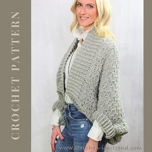 Könnte beinhalten: Eine Frau trägt eine hellgraue Häkeljacke über einem weißen Hemd und einer blauen Jeans. Die Strickjacke hat ein strukturiertes Muster und lange Ärmel. Die Worte "CROCHET PATTERN" sind vertikal auf der linken Seite des Bildes aufgedruckt.