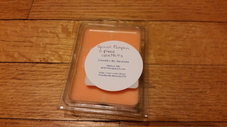Peut inclure: Gros plan sur un ensemble de 6 galets de cire dans un r&eacute;cipient en plastique transparent. Les galets de cire sont de couleur orange clair et portent une &eacute;tiquette indiquant "Spiced Pumpkin Wax Melts" et "Candles By Amanda".