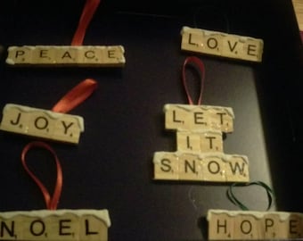 May include: A set of six Christmas decorations made from Scrabble tiles. The decorations spell out the words "PEACE", "JOY", "NOEL", "LOVE", "LET IT SNOW", and "HOPE".