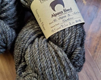Puede incluir: Una madeja de hilo de mezcla de alpaca gris con una etiqueta que dice "Alpaca Blend - small batch milled - Blend 70% Alpaca 30% Fine Wool - Shadow - 150 yards 7.1 oz 3 ply Bulky - farm to fiber - TCVT koby cottage vi"