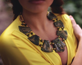 Puede incluir: Primer plano de una mujer con un top amarillo y un collar hecho de piezas con estampado verde y marrón con cuentas doradas.