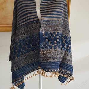 May include: A blue and gold striped shawl with geometric patterns and tassels. The shawl is draped over a white mannequin.