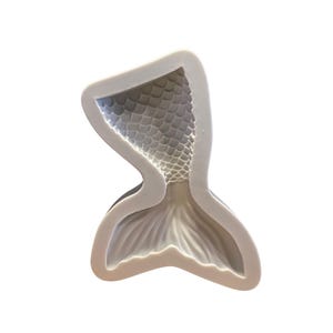 May include: A white silicone mould shaped like a mermaid tail with a detailed scale pattern.
