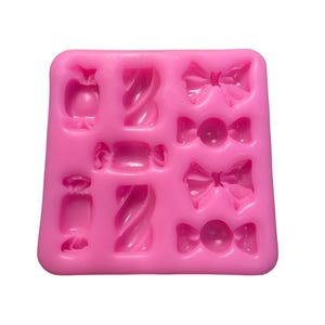 May include: Pink silicone candy mould with nine cavities. The cavities are shaped like bows, candy canes, and wrapped sweets.