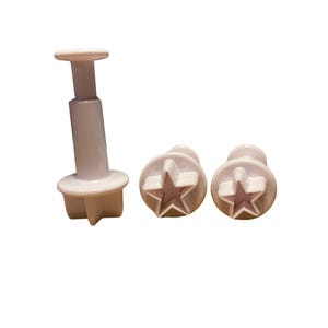 May include: Three white plastic cookie cutters, two are star shaped and one is a plunger cutter with a star shaped top.