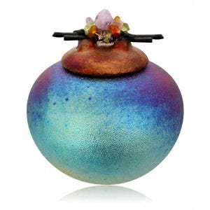 May include: A spherical ceramic vessel with a textured gradient finish transitioning from light blue to deep purple. The lid is a rounded copper-toned piece topped with a cluster of small, multi-colored gemstones and thin black horizontal sticks.