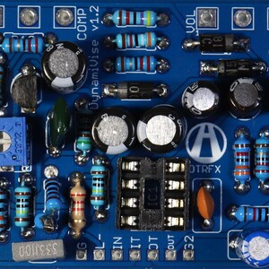 May include: A blue circuit board populated with electronic components such as resistors, capacitors, and an integrated circuit. The board is labelled "DynamiVise v1.2" and "OTRFX". The components are in various colours.