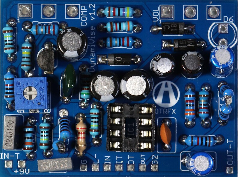May include: A blue circuit board populated with electronic components such as resistors, capacitors, and an integrated circuit. The board is labelled "DynamiVise v1.2" and "OTRFX". The components are in various colours.