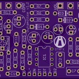 May include: A purple circuit board with white text and components. The board is labelled with text including "COMP DynamiVise v1.2", "RELEASE", and "OTRFX". It features numerous circular and square pads for soldering electronic components.