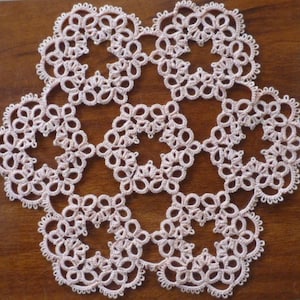 May include: A delicate white crocheted doily with a floral design. The doily is made of fine thread and has a circular shape.