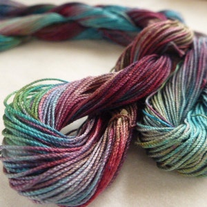 May include: A skein of colorful yarn in shades of teal, purple, green, and red. The yarn is tightly twisted, showing the individual strands. The yarn is likely used for knitting, crocheting, or other fiber arts projects.