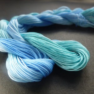Könnte beinhalten: Ein Knäuel blauer und türkisfarbener Stickgarn, verdreht und zu einem lockeren Knoten gefaltet.